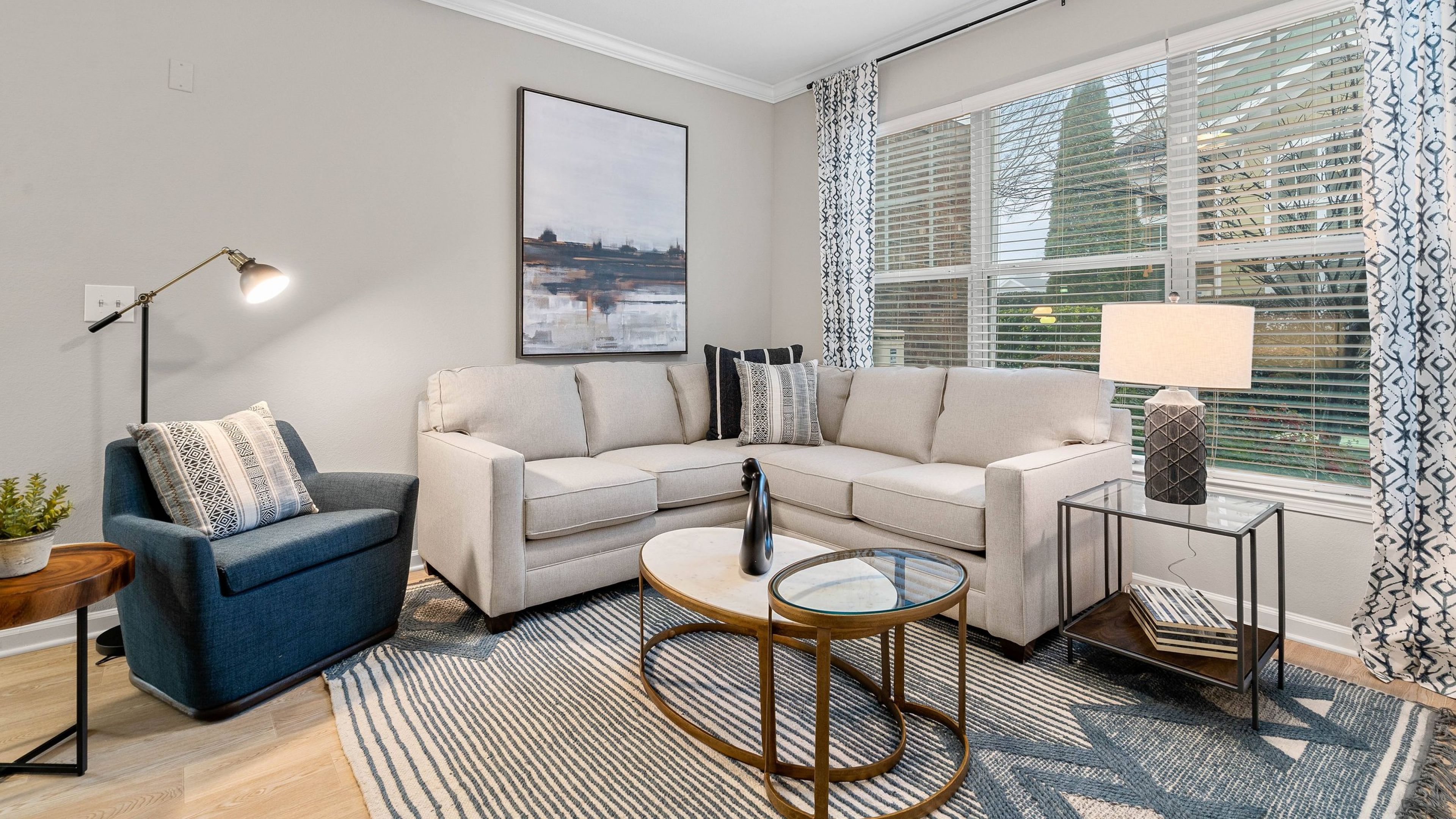 Hawthorne at the Greene apartment interior showing living room with large windows, a L shaped couch, chair, and coffee table