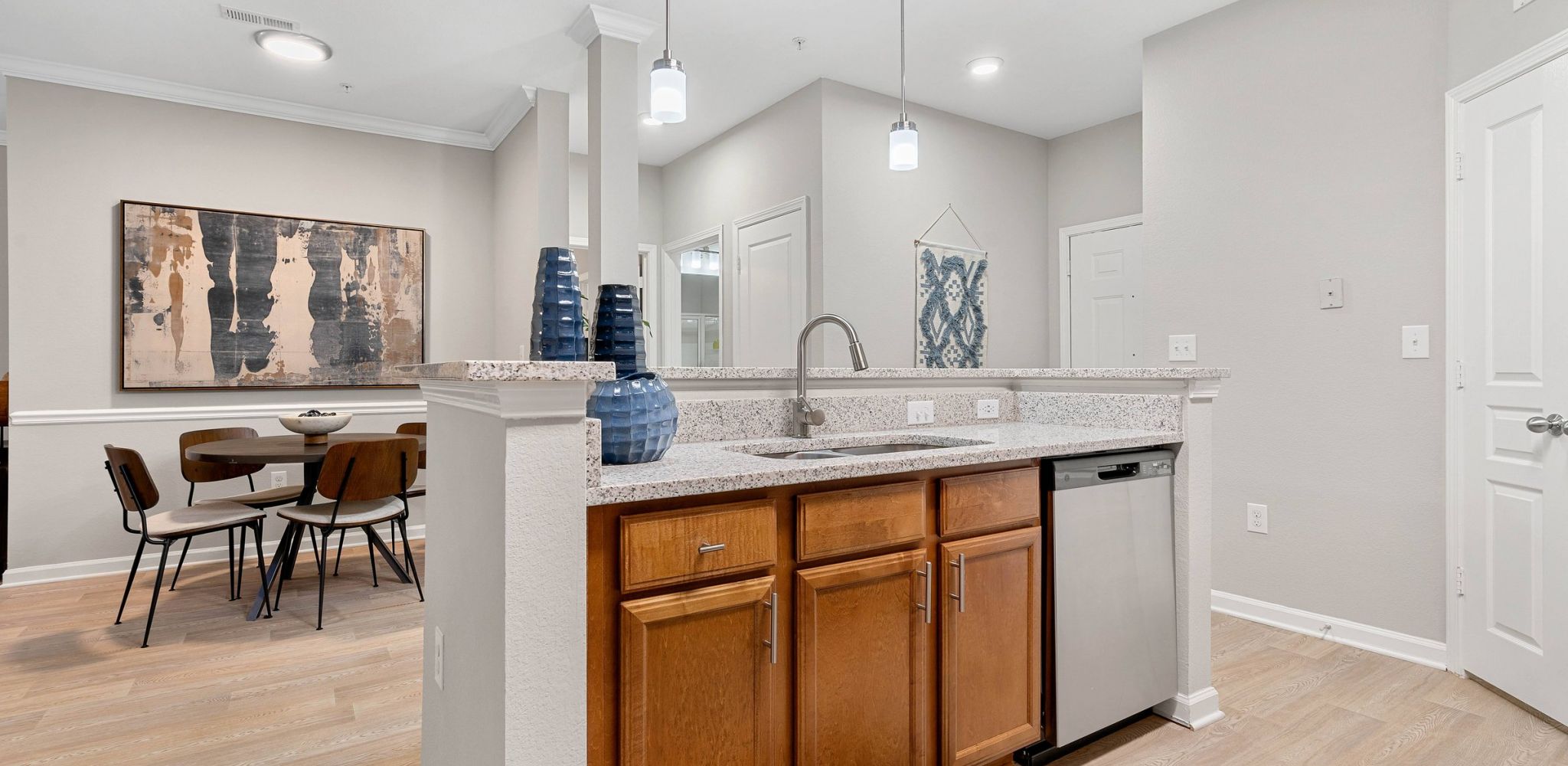 Hawthorne at the Greene apartment kitchen area looking towards kitchen island with sink, dishwasher, and counter space with a small dining table behind 